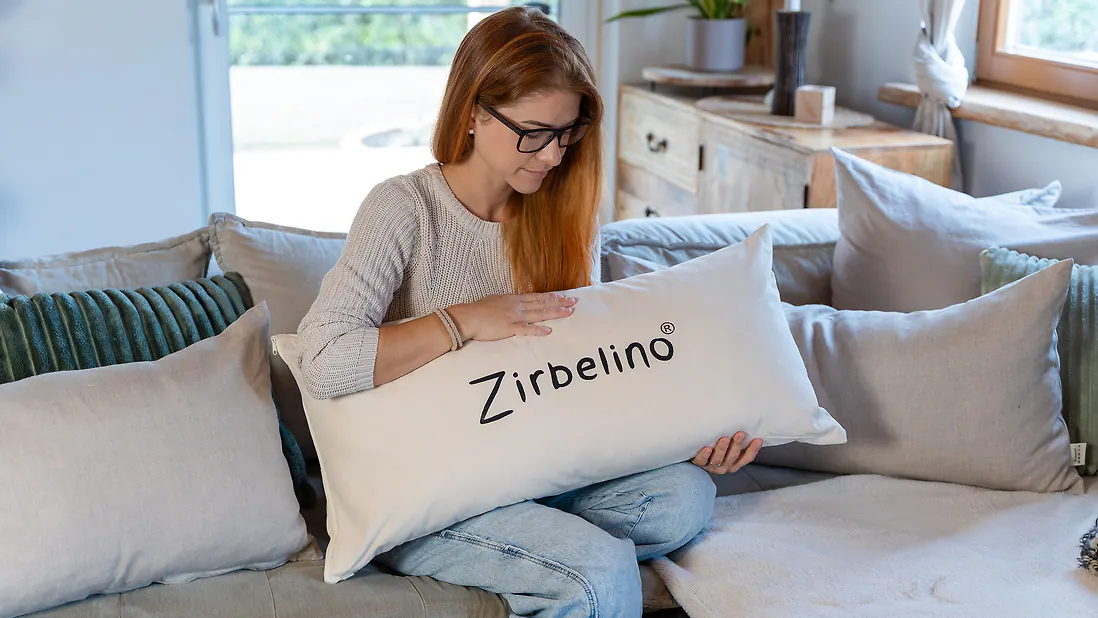 Frau auf Sofa hält großes Zirbelino Saunakissen aus Baumwolle
